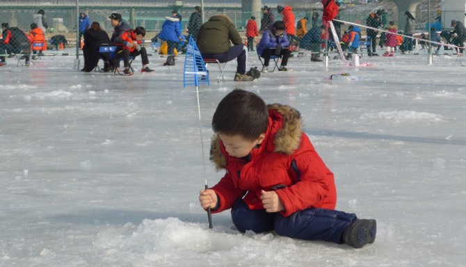 강원 영월군 영월읍 동강둔치에서 열린 제3회 영월동강 겨울축제장 얼음낚시터에서 한 어린이가 송어낚시의 즐거움에 빠져 얼음 구덩이를 바라보고 있다. 