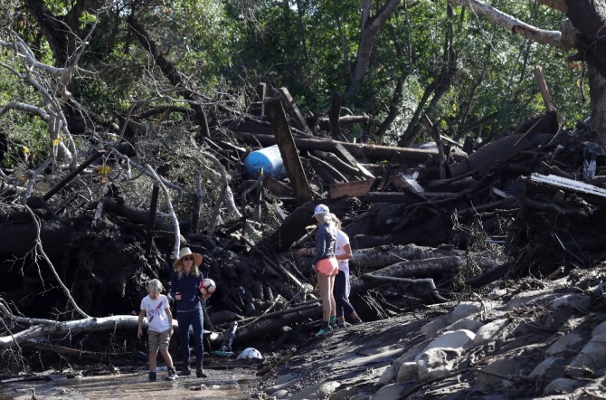 캘리포니아주 몬테시토에서 발생한 산사태로 떠내려온 나무 밑에서 한 가족이 걸어 나오고 있다. 이번 산사태로 10일(현지 시간) 현재 17명이 사망하고 12명이 실종됐다. 사진=AP/뉴시스