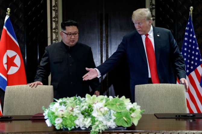 도널드 트럼프 미 대통령(오른쪽)이 12일 싱가포르 센토사섬의 카펠라 호텔에서 열린 김정은 북한 국무위원장과의 사상 첫 북미 정상회담 후 합의문에 서명하기에 앞서 김 위원장에게 자리에 앉으라고 권하고 있다.뉴시스