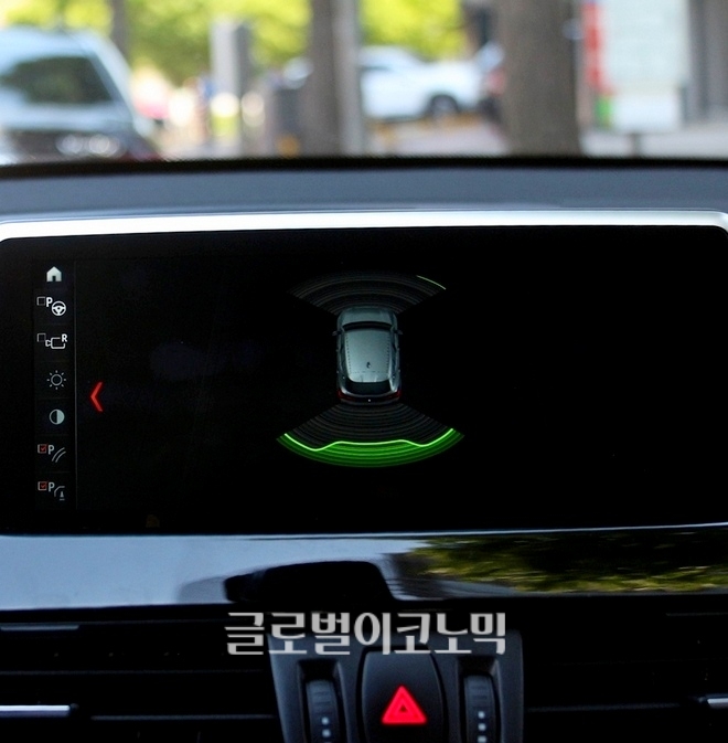 X2 M의 13인치 LCD에는 차량의 각종 기능 조작 상황이 표시된다. LCD에 차량 후면에 물체가 있고, 후진 시 차량 우측 앞뒤에 위험을 알리고 후방 모습을 비추고 있다.