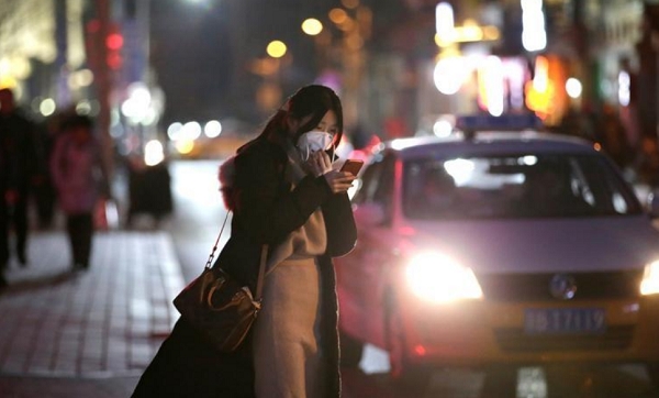 중국 베이징에서 저녁에 한 여성이 마스크를 쓴 채 스마트폰을 보고 있는 모습. 사진=로이터