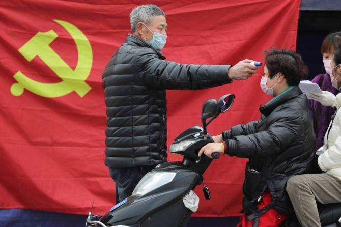 중국 동부 저장성 대도시에서 지난 3일 공산당 기 앞에서 한 자원봉사자가 도로변 검역 포인트에 온 스쿠터 운전자의 체온을 재고 있다. 사진=뉴시스