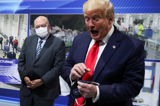 도널드 트럼프 대통령이 지난 21일(현지시간) 미국 미시간주 소재 포드차 공장을 짐 해킷 CEO의 안내로 시찰하던 중 뒤쪽에서 마스크를 착용했지만 카메라 앞에서는 마스크를 쓰지 않는 이유에 대해 설명하고 있다. 사진=로이터