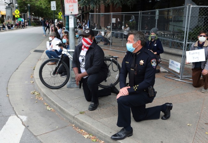 미 캘리포니아주 산타크루즈의 앤디 밀스(오른쪽)경찰서장이 저스틴 커밍스(가운데) 산타크루즈 시장과 함께 한 쪽 무릎을 꿇고 있다. 이들은 인종차별 반대 시위를 진압하는 대신 시민들과 뜻을 함께 하겠다고 밝혔다.사진=뉴시스