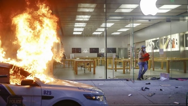 미국 필라델피아의 애플스토어 매장앞에서 경찰차가 불에 타고 있는 가운데 한 흑인이 매장을 나오고 있다. 필라델피아=AP/뉴시스