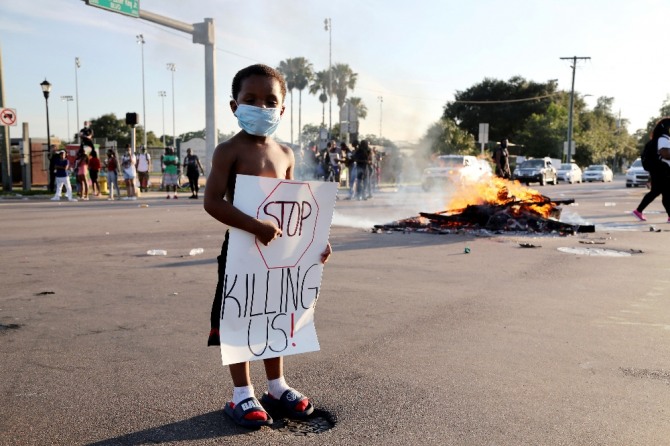 31일(현지시간) 미국 플로리다주 탬파에서 5세 흑인 아이가 시위로 폐쇄된 도로에서 우리를 그만 죽여라!고 적힌 종이를 들고 있다.  AP/뉴시스