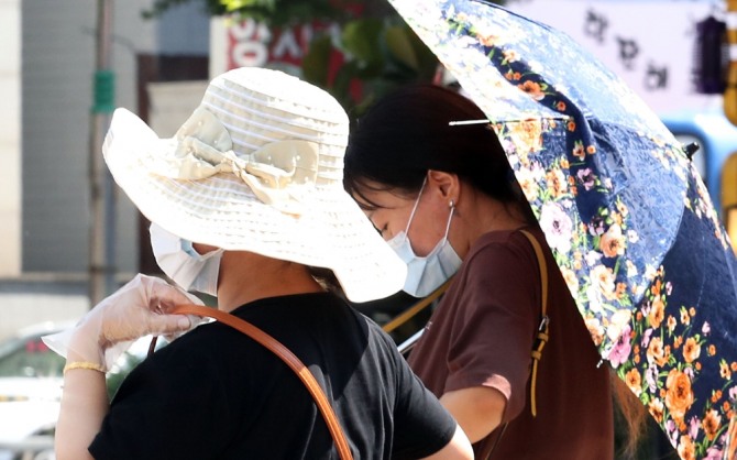 위생장갑을 끼고 마스크 쓴 시민이 양산과 모자를 쓰고 도로를 걸어가고 있다. 사진=뉴시스