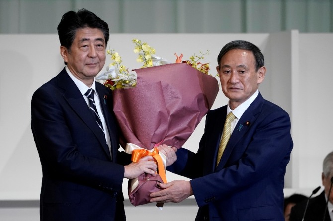 아베 신조 일본 전 총리(왼쪽)가 14일 도쿄의 한 호텔에서 열린 자민당 총재 선거에서 총재로 선출된 스가 요시히데 관방장관에게 꽃다발을 건네며 축하하고 있다. 사진=AP/뉴시스