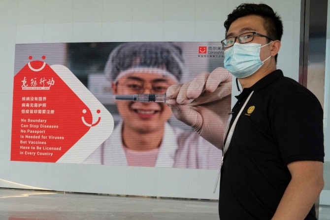 24일 중국 제약회사 시노백의 베이징 공장에서 한 직원이 코로나19 광고판 앞에 서 있다.  AP/뉴시스