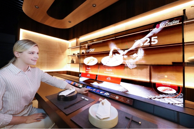 한 여성이 LG디스플레이가 ‘CES 2021’에서 선보이는 ‘레스토랑 존’을 찾아 투명 OLED를 이용해 메뉴를 살펴보고 있다. 사진=LG디스플레이