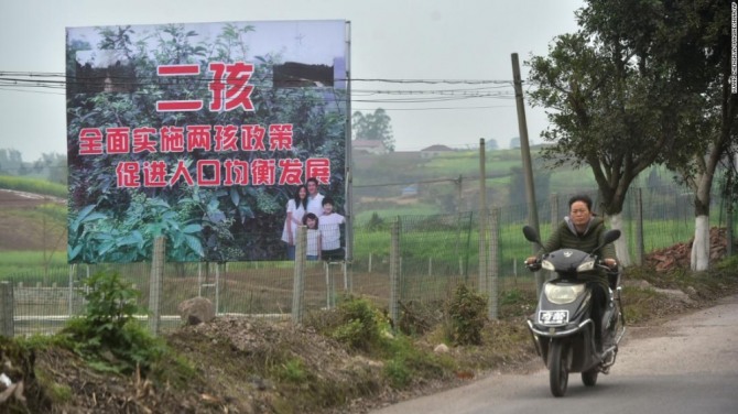 지나 2017년 3월 23일 중국 쓰촨성 네이장에 있는 2자녀 출산 장려 공익 광고판 앞을 직장인으로 보이는 여성이 스쿠터를 타고 지나가고 있다. 사진=CNN
