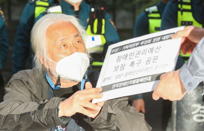 지난 23일 오후 박경석 전국장애인차별철폐연대(전장연) 대표가 서울 강남구 추경호 기재부장관 후보자 자택 인근에서 열린 '장애인권리예산 보장 약속 공문전달 기자회견'에서 아파트 관리과장에게 공문을 전달하고 있다. 박 대표는 25일 지하철 출근길 집회를 유보하겠다고 말했다. 사진=뉴시스