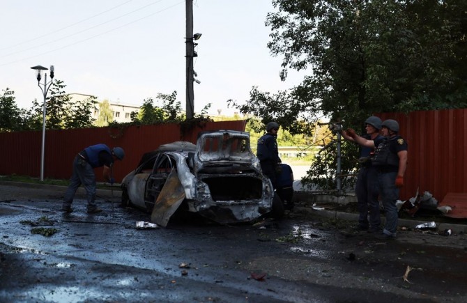 러시아의 공습으로 파괴된 차량 옆에서 조사를 하고 있는 우크라이나 경찰관. 사진=로이터