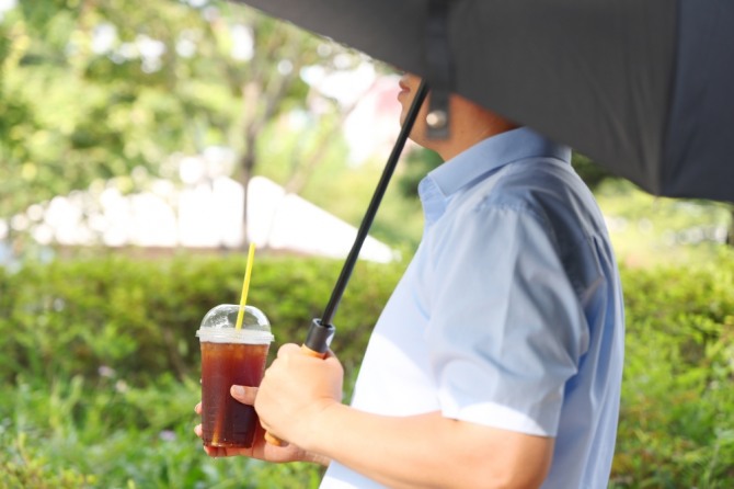 찜통더위가 이어진 지난달 31일 오후 한 직장인이 수성구 한 도로에서 햇볕을 가리기 위해 우산을 쓰고 얼음 음료를 마시며 걸어가고 있다. 사진=연합뉴스.