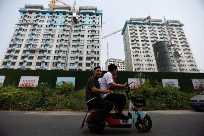 중국 베이징에서 건설 중인 주거용 건물을 지나가는 사람들이 스쿠터를 타고 있다. 사진=로이터