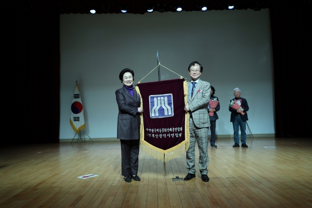 부산시 남구 용소로에 위치한 부산예술회관 1층 공연장에서 22일 오후 개최된 '제63차 정기총회와 제27대 임원 선거'에서 부산예총 차기 회장으로 당선된 오수연(왼쪽) 후보가 안규성 선관위원장으로부터 예총기를 전달받고 있다. 사진=부산예총 제공