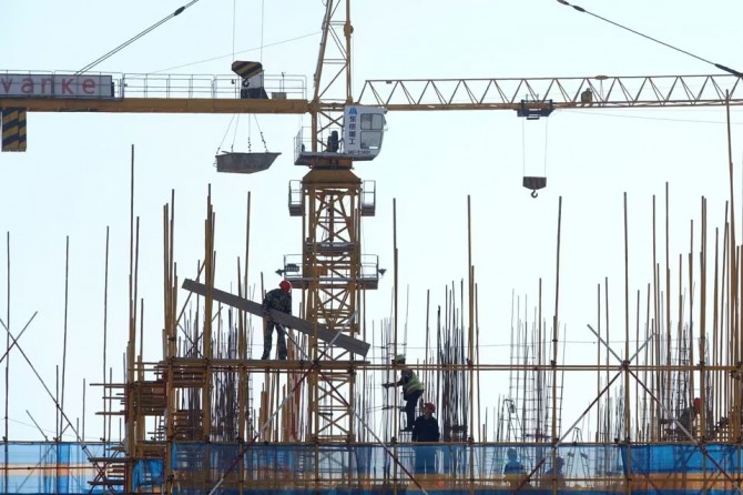 중국 랴오닝성 다롄의 한 주거용 건물 건설 현장에서 일하는 노동자들 위에 부동산 개발업체 완커의 간판이 보인다. 사진=로이터
