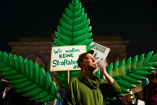 지난달 1일(현지시각) 독일 베를린의 브란덴부르크 문에서 독일의 대마초 친구들이 대마초 합법화를 흡연으로 축하하는 동안 한 남자가 '우리는 범죄자가 되고 싶지 않습니다'라고 적힌 표지판 앞에서 담배를 피우고 있다. 사진=로이터