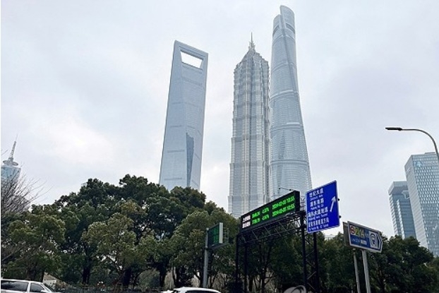 2024년 2월 5일 중국 상하이의 루자쭈이 금융 지구에 있는 상하이 타워와 다른 고층 빌딩들 근처에서 차량들이 상하이 및 선전 주가지수를 보여주는 전광판을 지나가고 있다. 사진=로이터/연합뉴스