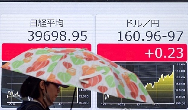 2024년 6월 28일 도쿄 증권거래소의 미국 달러 대비 엔화 환율(오른쪽)과  닛케이 지수(왼쪽) 전광판 앞을 한 사람이 우산을 쓰고 지나가고 있다. 사진=AFP/연합뉴스