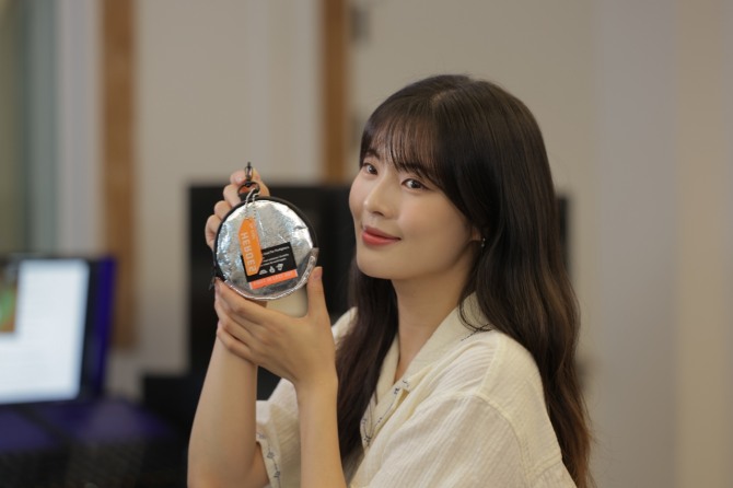 배우 이선빈이 ‘국민히어로즈’ 캠페인 리워드인 업사이클링 파우치와 넘버링 키링을 들고 사진촬영을 하고 있다.  /사진=희망브리지