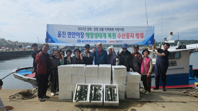 울진 연안어장 해양생태계 복원 수산종자 방류에 참여한 어촌계 주민들이 방류 전 전복 종자를 앞에 두고 기념촬영을 하고 있다.  /사진=희망브리지