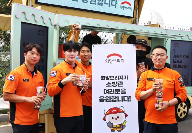 청주국제공항 긴급구조종합훈련 현장에서 소방대원들이 희망브리지 간식 지원 후 음료와 컵과일을 들고 기념촬영을 하고 있다. 사진=희망브리지